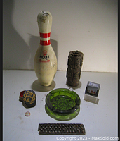 Photo showing the full vintage Brunswick Mixer bowling pin, carved wooden item, decorative box, green glass ashtray, small metal grater, and pin button.