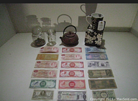 Full lot showing Japanese teapot, tea cup on decorative box, two glass jars with coins, and 13 vintage banknotes.