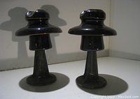 Two large vintage black ceramic and steel insulators on a white background.