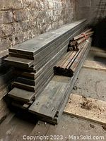 Side view of stacked reclaimed Ipe decking boards stacked against a brick wall with pre-drilled holes.