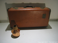 Closed outside view of the brown Martin trumpet case alongside a copper trumpet mute.