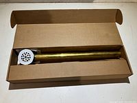Tub drain assembly in box showing perforated top cover and brass-colored cylindrical body.