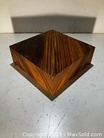 Square wooden pedestal with wood grain pattern, shown from a top corner angle to highlight wood texture and finish.