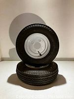 Photo showing two black trailer tires with zigzag tread pattern mounted on white steel rims with five lug nut holes each.