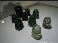 Nine vintage insulators arranged on white surface showing clear, green glass and dark brown/black ceramic insulators.