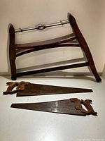 Three vintage saws laid out flat on a white surface. Includes a wooden bow saw, a hand saw with wooden handle, and a smaller hand saw.