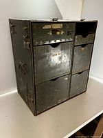 Front view of olive drab metal cabinet with four drawers and two smaller compartments, showing military markings and wear