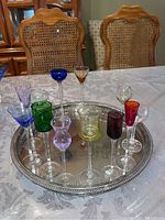 Set of 12 assorted colored liqueur/shot glasses arranged on an oval silver tray on a dining table