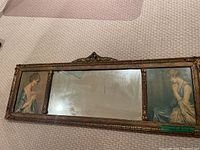 Full view of the horizontal antique mirror showing the decorative frame and two painted portrait panels on either side of the smoky mirror glass.