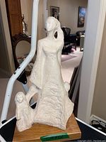 Front angled view of white sculpture of mother with children, mounted on wooden block.