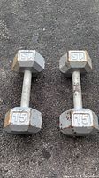 Photo showing two 15 lb cast iron hex dumbbells side by side on asphalt surface, visible rust and wear.