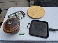 Overview of all four items on table including square cast iron skillet, brown crock with lid, divided stainless steel tray, and wooden lazy susan.