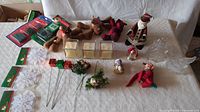 Photo showing entire assortment of Christmas decorations on a table including plush toys, metal Santa, candle holders, wreaths, and small decorative items