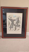 Framed lithograph showing full view of wooden frame with black and red mat around the print depicting two dancing rabbis.