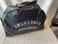 Front view of the black Lululemon Athletica gym bag with white logo lettering.