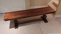 Front angle view of the walnut wood bench showing length and pedestal supports