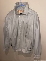Full view of cream-colored men's leather jacket on hanger showing front and collar with elastic waistband and cuffs.