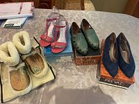 Four pairs of ladies shoes on table including fluffy CicciaBella booties, pink satin sandals, green leather espadrilles, and navy suede pumps on boxes