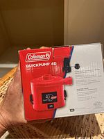Front view of Coleman QuickPump 4D red and black air pump box showing product image and branding.