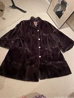 Front view of vintage dark brown sheared beaver fur swing coat with pearl-like buttons and collar laid flat on carpet.