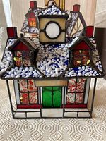 Front view of Tiffany Gallery Christmas lighthouse stained glass lamp showing colorful glass panels with red roofs, green door, and white-blue snowy roof details.