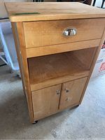 Full view of wooden cabinet showing the top drawer with metal handle, open shelf, and double-door storage area below with wooden knob handles. Cabinet is on caster wheels.