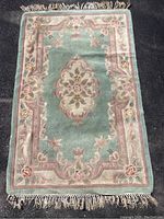Front view of wool rug showing moss green background and dusty rose floral emblem in center, floral border, fringe edges