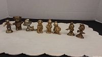 Full view of all 8 brass figurines arranged in a row on white cloth with plain background