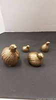 Four brass partridge figurines arranged on black surface showing scale and detail.
