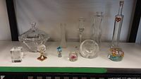 Lot overview showing entire glass and crystal decor items including candy dish, vases, paperweights, and figurines arranged on white shelf.
