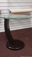 Side view of the oval glass top and curved black wooden leg of side table