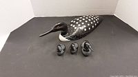 Large black and white hand carved loon with red eyes and three smaller loons in front on a black surface