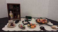 Wide view showing a wooden display shelf with ceramic Santa figure and several miniature trays and baskets with assorted miniature fruits and vegetables, placed on white cloth.