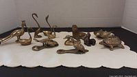 Photo showing all 11 brass animal figurines including birds, seals, ducks, lobster, turtle with opener, and shell-shaped item, arranged on white cloth background.