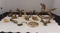 Photo showing full collection of miniature brass animal figurines laid out on a white surface, including the rocking horse, camel, mouse, rabbits and other animals