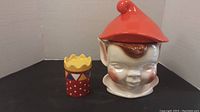 Large pixie cookie jar and small colorful canister placed side by side on a plain background