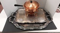 Copper fondue pot placed on top of two large silver-plated trays showing overall lot composition