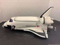 Side view of the US Space Shuttle cookie jar showing the intact body, windows, and decals including 'United States' and the flag.