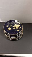 Stack of 7 cobalt blue plates with gold bird and floral decorations visible on top plate, edges with gold rim