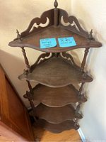 Front view of the antique wooden corner shelf showing four shelves, scalloped edges, turned spindles, and decorative cutout backs.