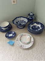 Photo showing the full display of blue flow and white with floral accent dishes on carpet, including bowl, plates, and covered dish.