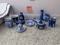 Photo showing a variety of blue and white Wedgwood jasperware pottery and decorative items arranged on carpet with a note reading 'blue glasourer'