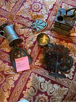 Overview of cast iron items on patterned cloth including tractor figurine, cup, small pitcher, and decorative small oven piece.