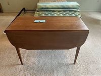Front view of the wooden drop leaf table with one leaf down showing the natural wood finish and tapered legs.