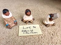 Three Eskimos figurines displayed on beige carpet next to handwritten note with lot title and artist name