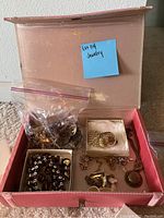 Open pink jewelry box with assorted costume jewelry pieces including brooches, necklaces, earrings, and rings