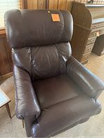 Brown leather recliner chair with padded arms and cushioned backrest, showing some wear and wrinkling on the leather surface.
