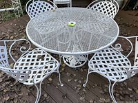 White iron round table with four matching chairs outdoors on a deck, showing round lattice metal tabletop and details of chairs.