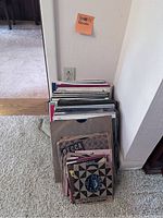 Image showing a large stack of vinyl LP records and a smaller pile of 45 RPM records leaning against a wall.
