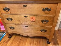 Front view showing three drawers and ornate antique-style metal hardware on red maple dresser.